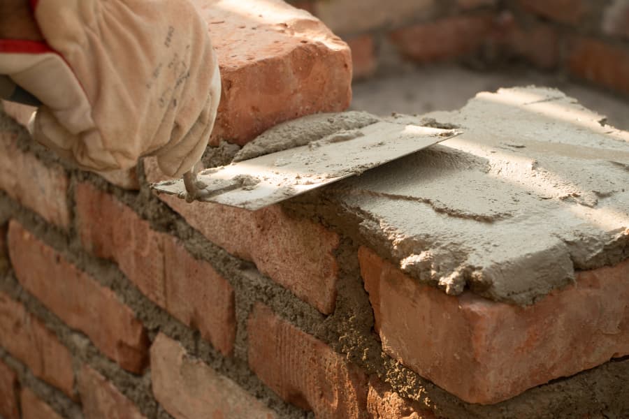 Close image of mason using trowel to spread mortar on brick